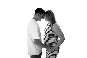 Black and white photo of a pregnant couple touching foreheads, woman in striped dress cradling baby bump.