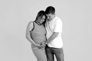 Black and white maternity photo of a couple tenderly looking down at the pregnant woman's baby bump in a studio.