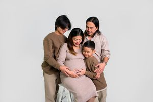 Pregnant woman surrounded by family members in matching beige outfits posing for a maternity photo.