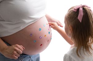 Young girl decorating pregnant mother's belly with colorful gem stickers in a sweet bonding moment.