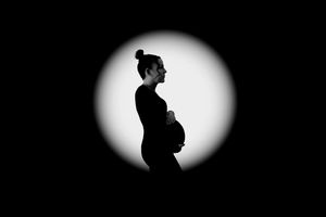 Black and white silhouette of a pregnant woman cradling her baby bump in a circular spotlight.
