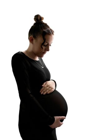 Pregnant woman in black dress cradling her baby bump against a white background.