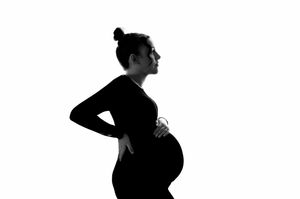 Black and white silhouette of a pregnant woman in profile, cradling her baby bump against a white background.