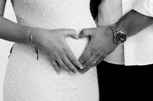 Couple forming a heart shape with hands on pregnant belly in black and white maternity photo.
