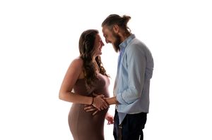 Pregnant couple holding baby bump together in a romantic maternity photo shoot against white background.