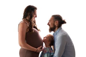 Pregnant woman with toddler and bearded man in studio maternity family portrait on white background.