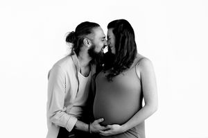 Black and white maternity photo of a couple kissing while the pregnant woman cradles her baby bump.