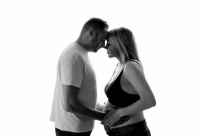 Black and white maternity photo of couple touching foreheads, man holding pregnant woman's belly in studio.