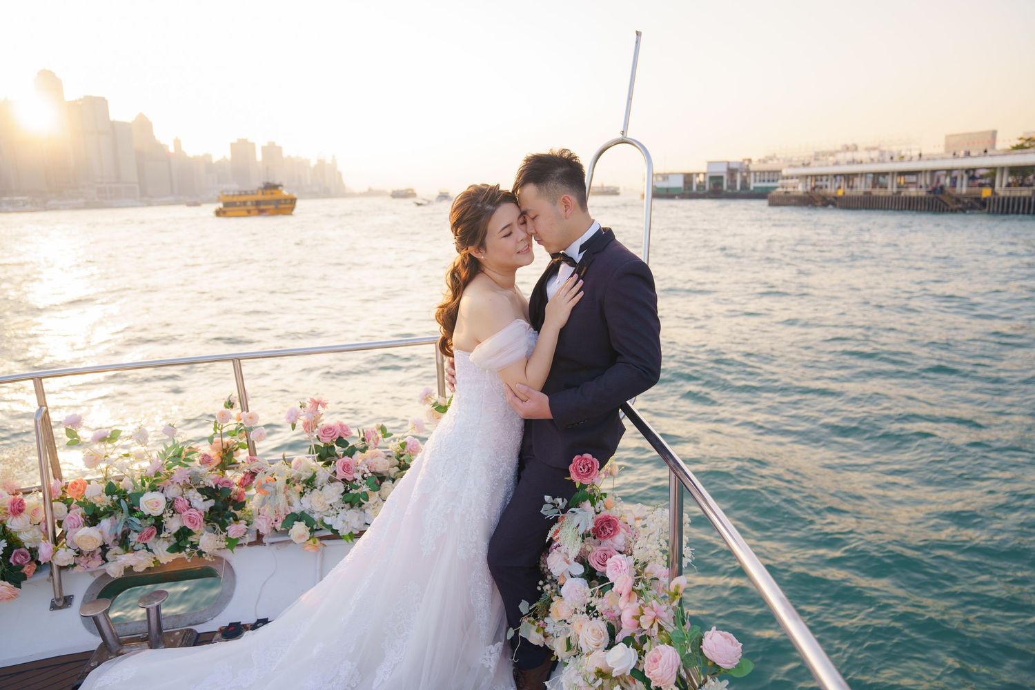 A romantic sunset boat wedding with pink and white floral arrangements, overlooking a coastal cityscape on the water.