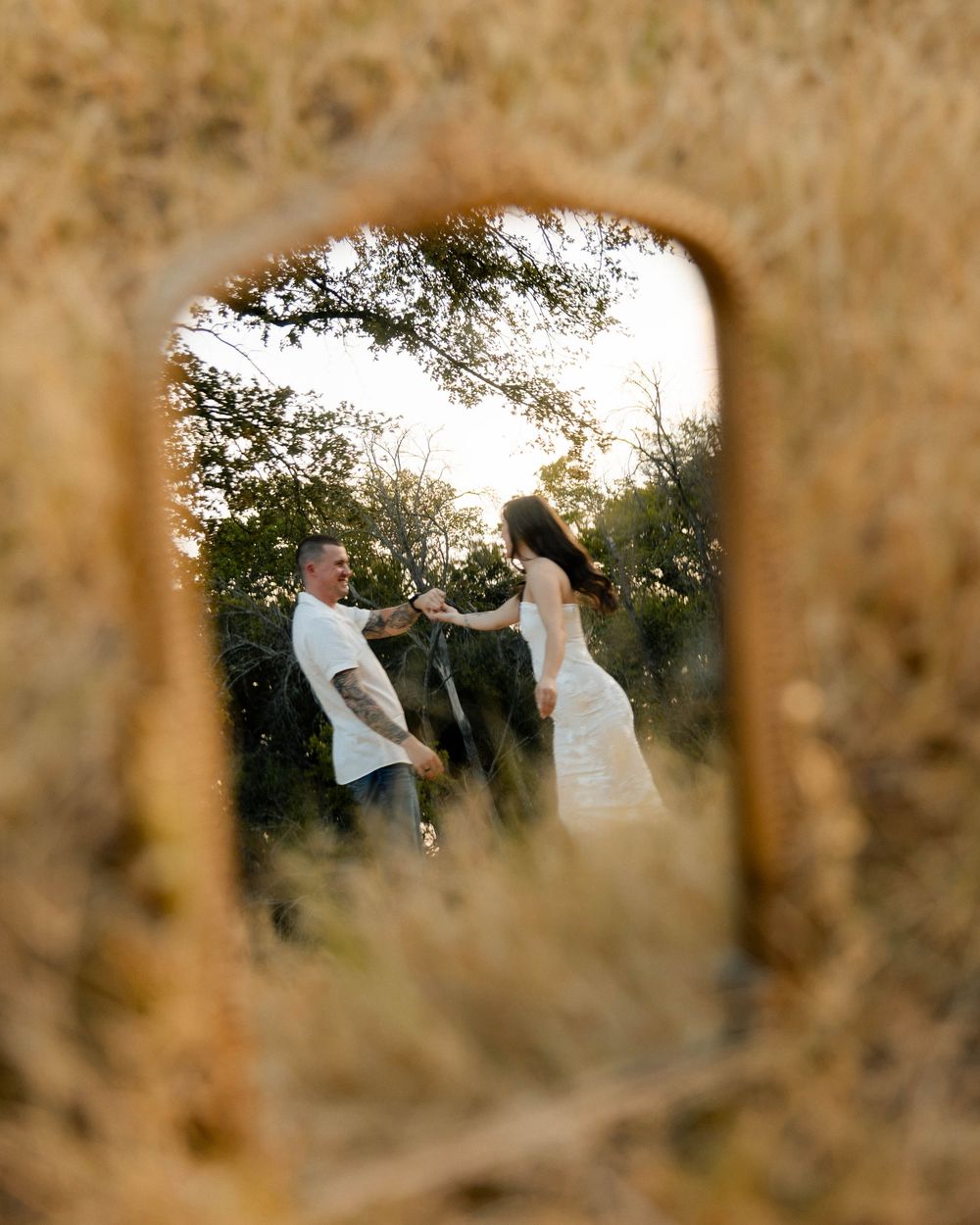 A couple dances in golden fields, captured through a mirror reflection, bride in white dress, groom in white shirt.