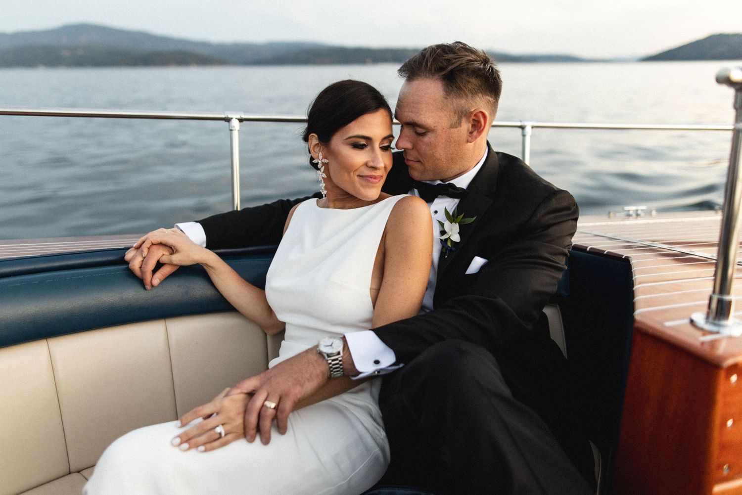 Bride and groom sitting closely together on a luxury boat on the water at dusk.