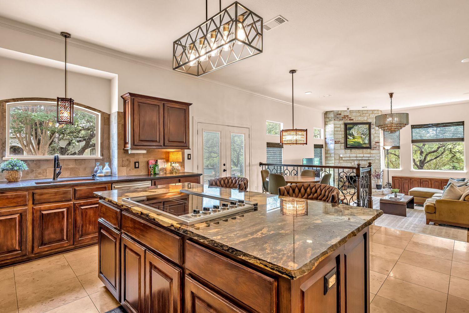 Elegant kitchen with granite island, cherry wood cabinets, chandelier lighting, and open layout flowing into a spacious living area.