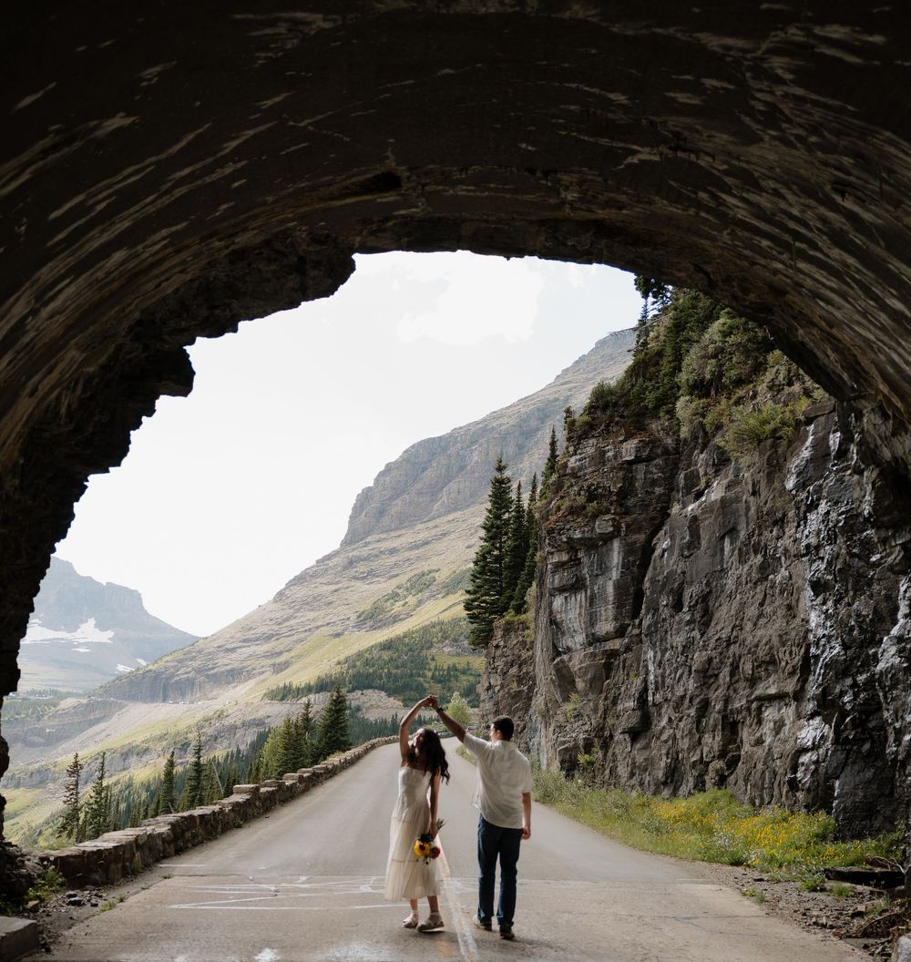 Couple dances under stone tunnel arch with breathtaking mountain valley view ahead.