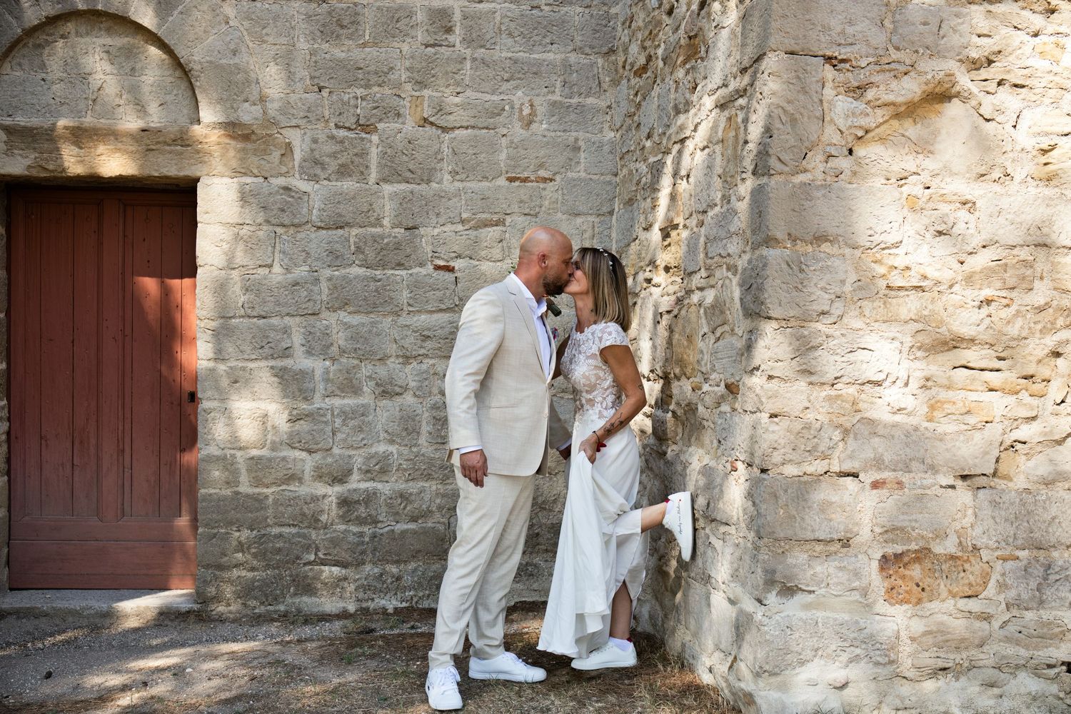 Delphine et Christophe s’embrassent contre un mur de pierre, à côté d’une porte ancienne.