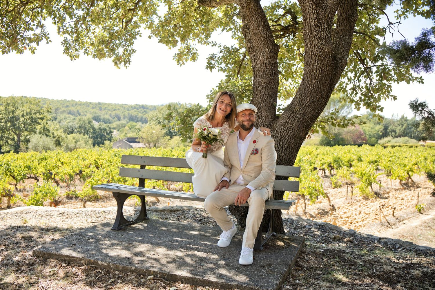 Les mariés prennent un moment à deux sur un banc à l’ombre d’un arbre, près des vignes.