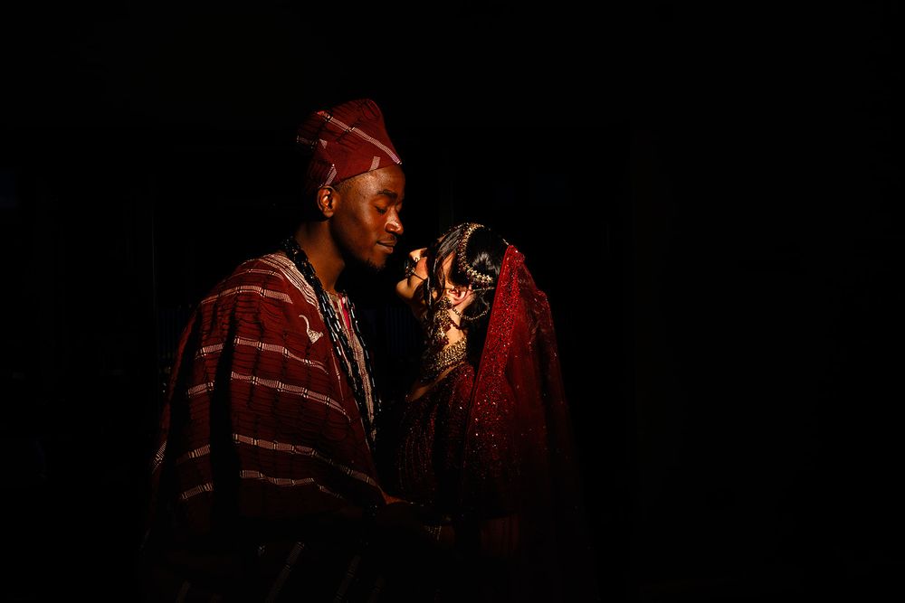Man in a red striped traditional robe and cap gazes at an ornate beaded and embroidered garment against a dark background.