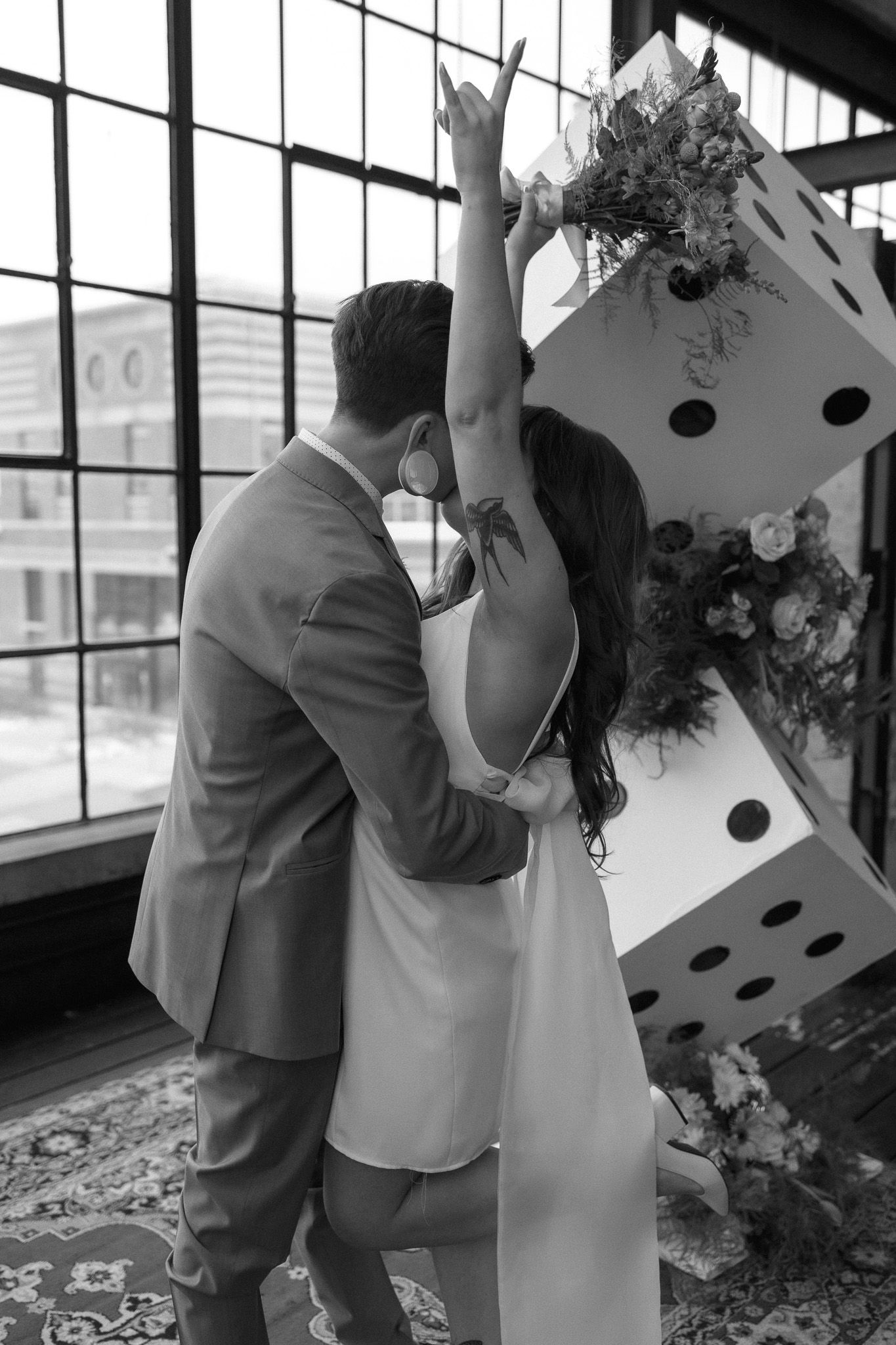 Black and white photo of a large decorative dice with floral arrangements in an industrial space.