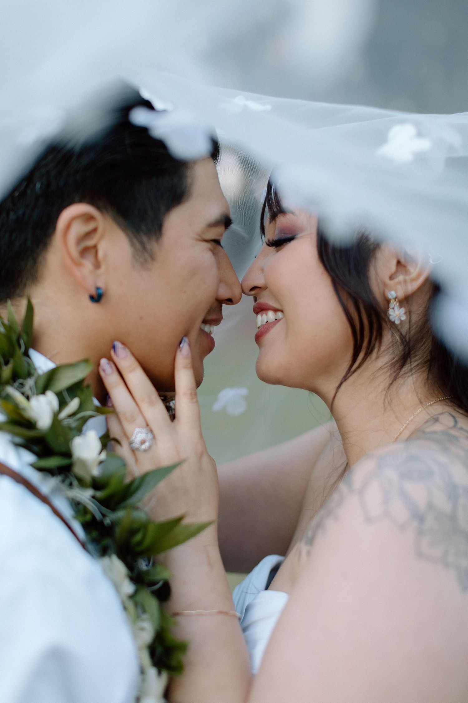 Romantic wedding portrait of couple under veil with white flowers.