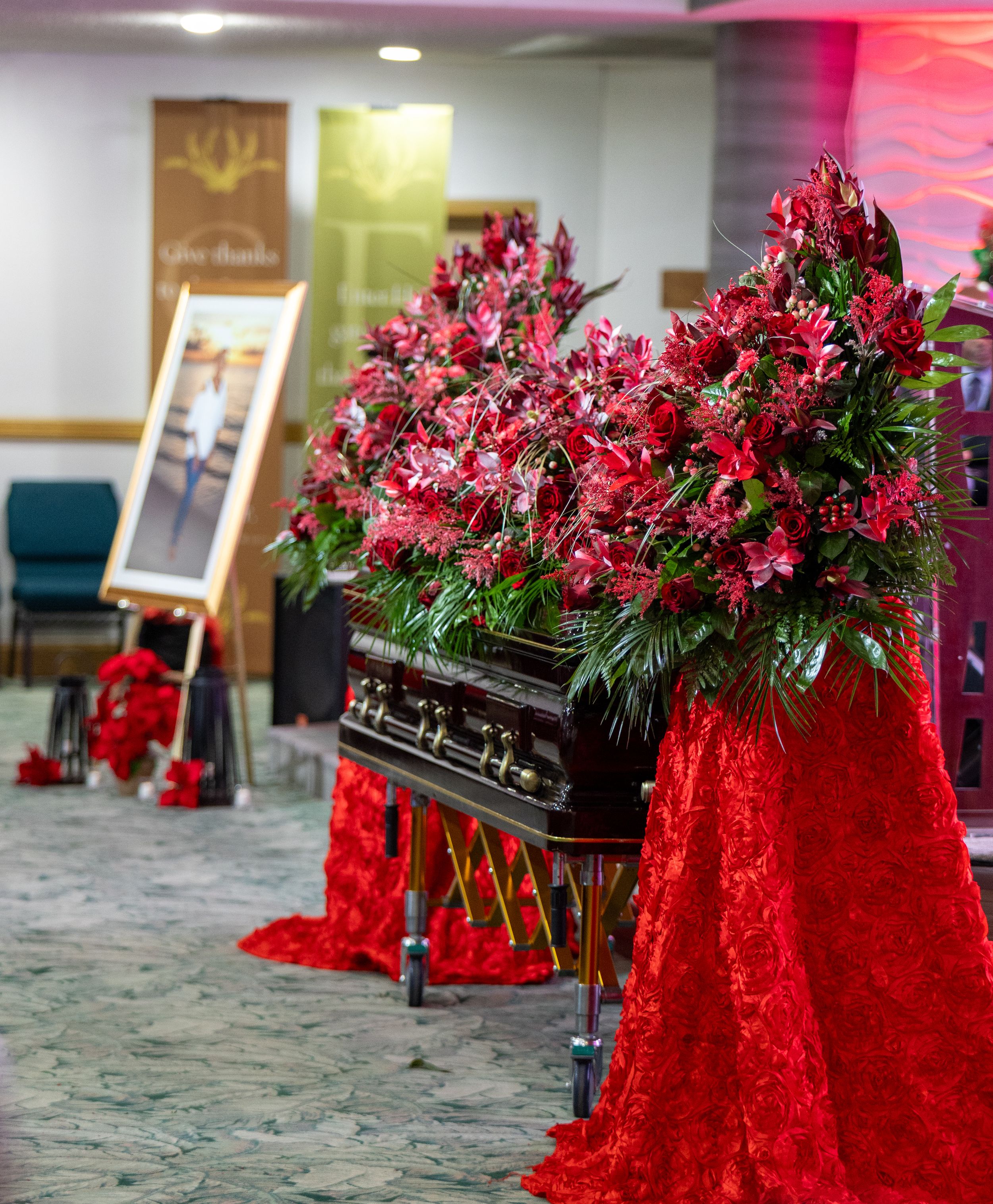 Multiple caskets decorated with red flowers and velvet draping in a memorial service hall.