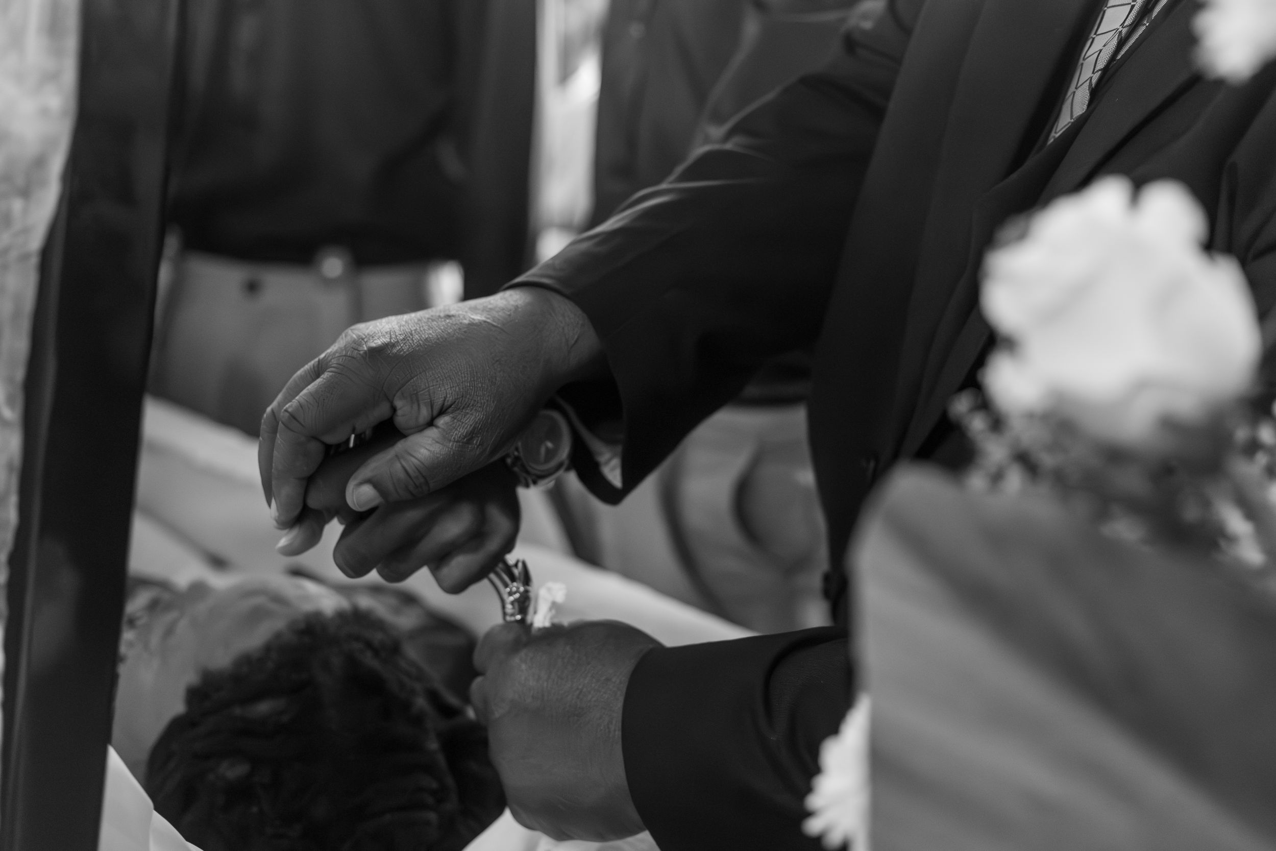 Black and white wedding photo of groom placing ring on bride's finger during ceremony.