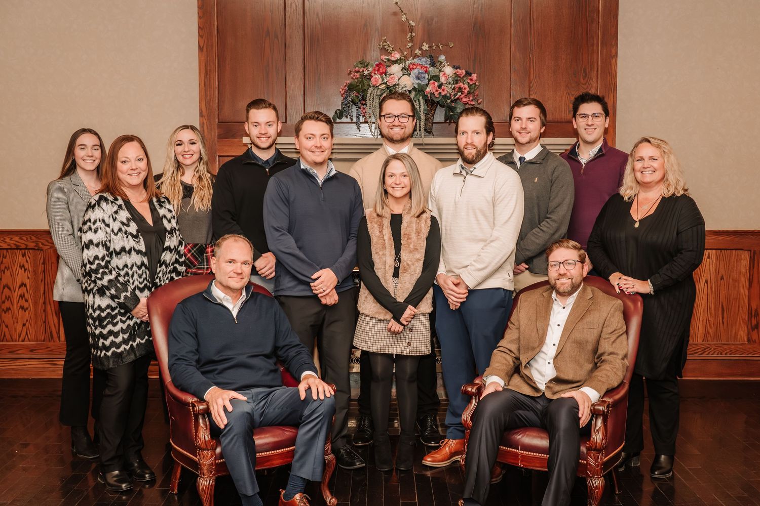 A large group of people pose together in a formal setting with wood paneled walls and warm lighting.