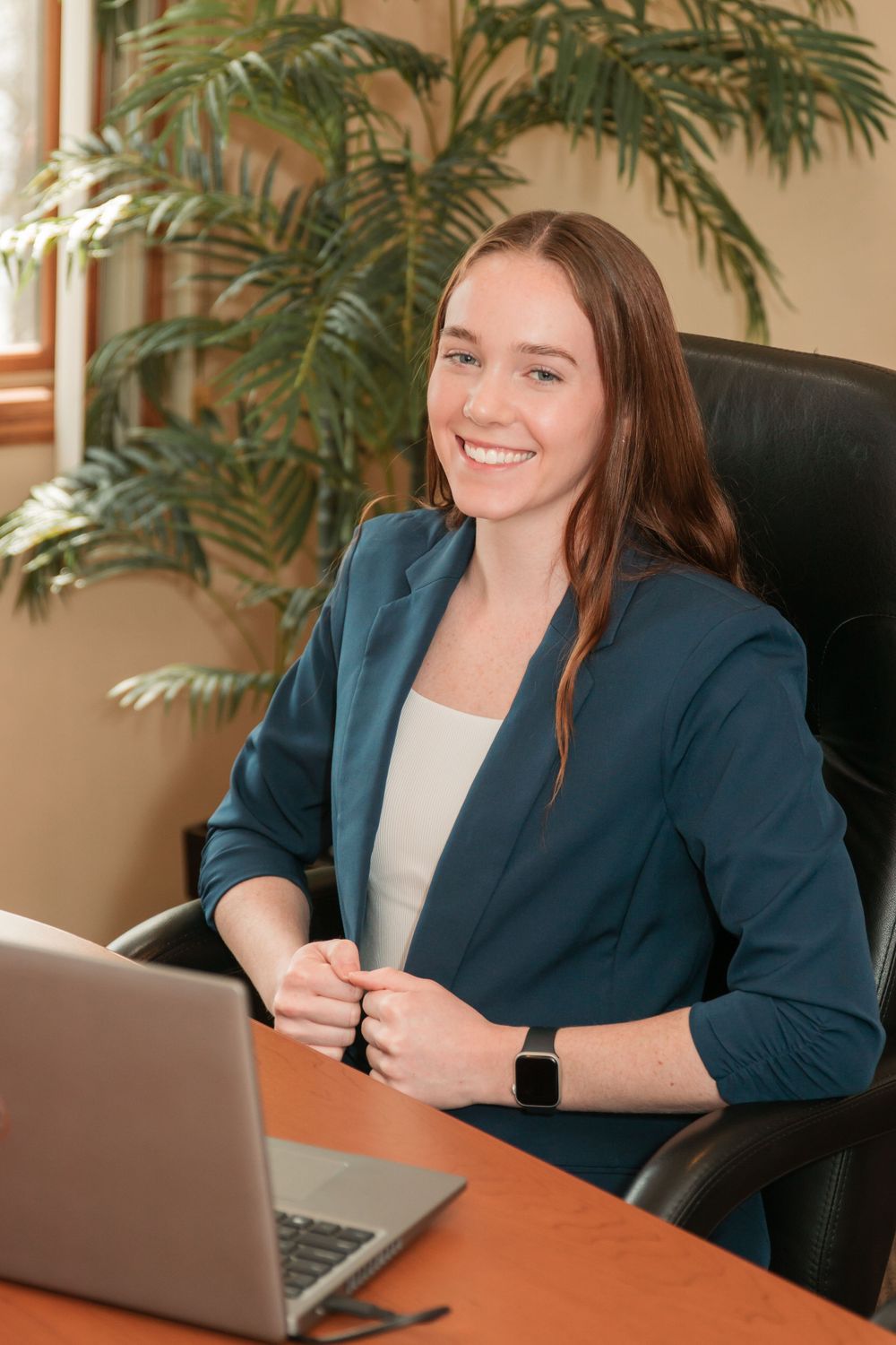 Professional workspace scene with laptop on wooden desk and indoor palm plant.
