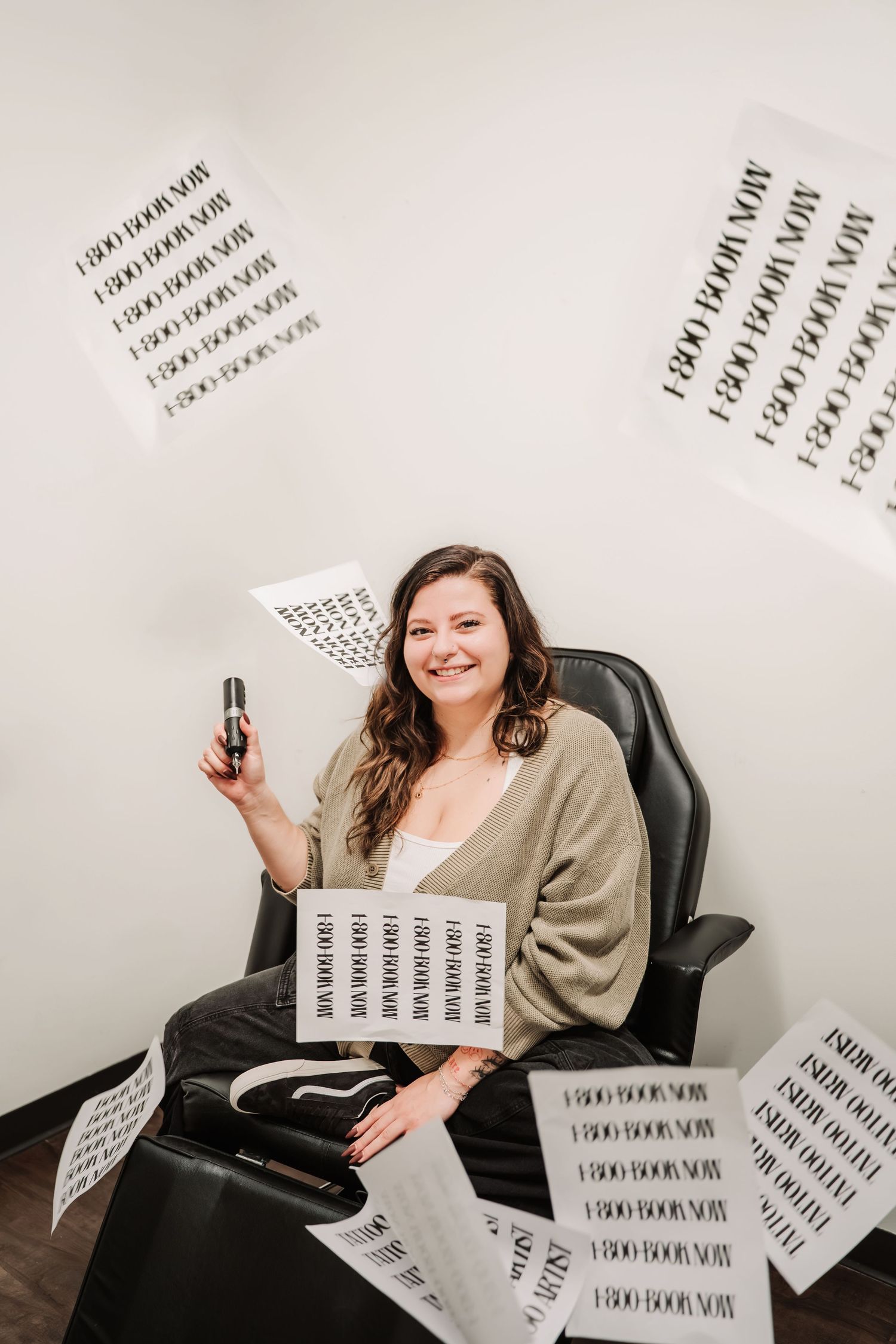 Woman smiling in office chair surrounded by flying '1-800 Book Now' papers, holding a phone in a fun promotional photo.