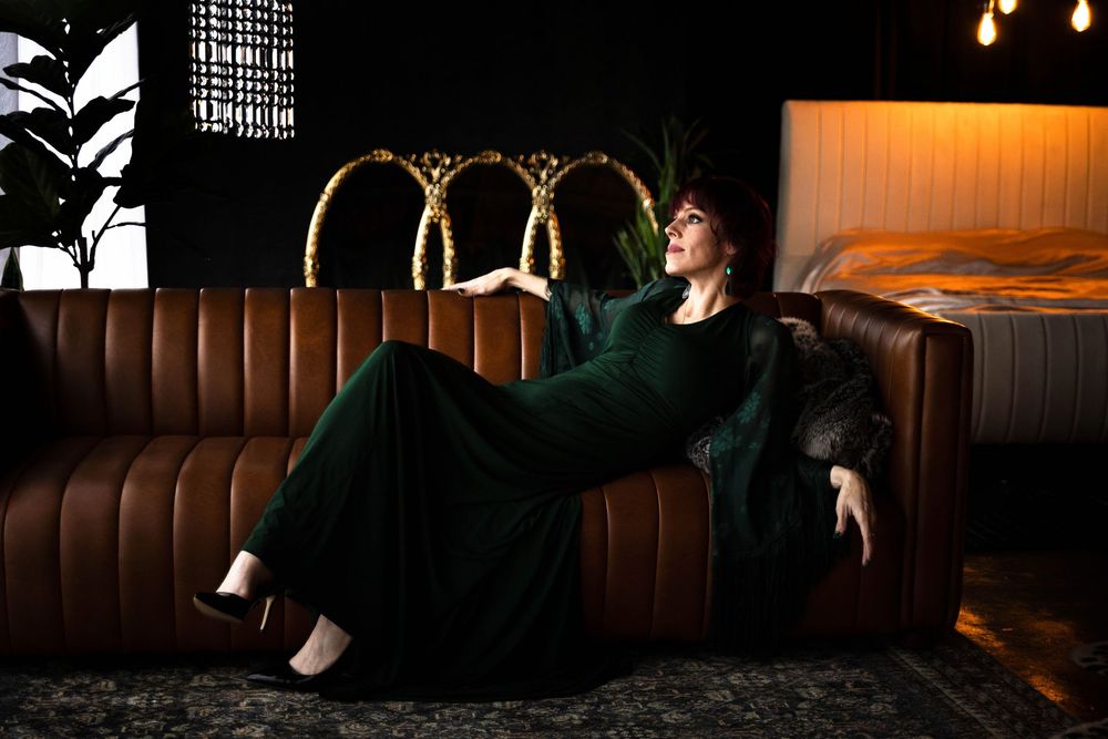 A woman in a green dress poses on a brown couch.