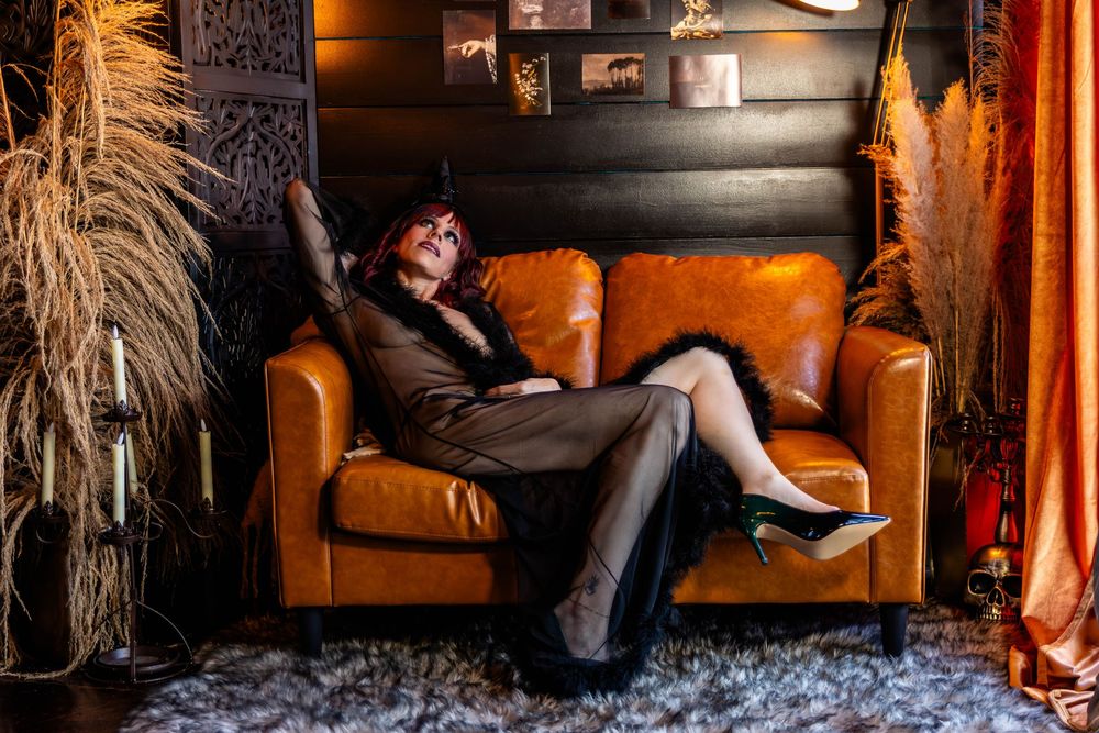 A woman with red hair and wearing a shear black robe poses sensually on a brown couch.