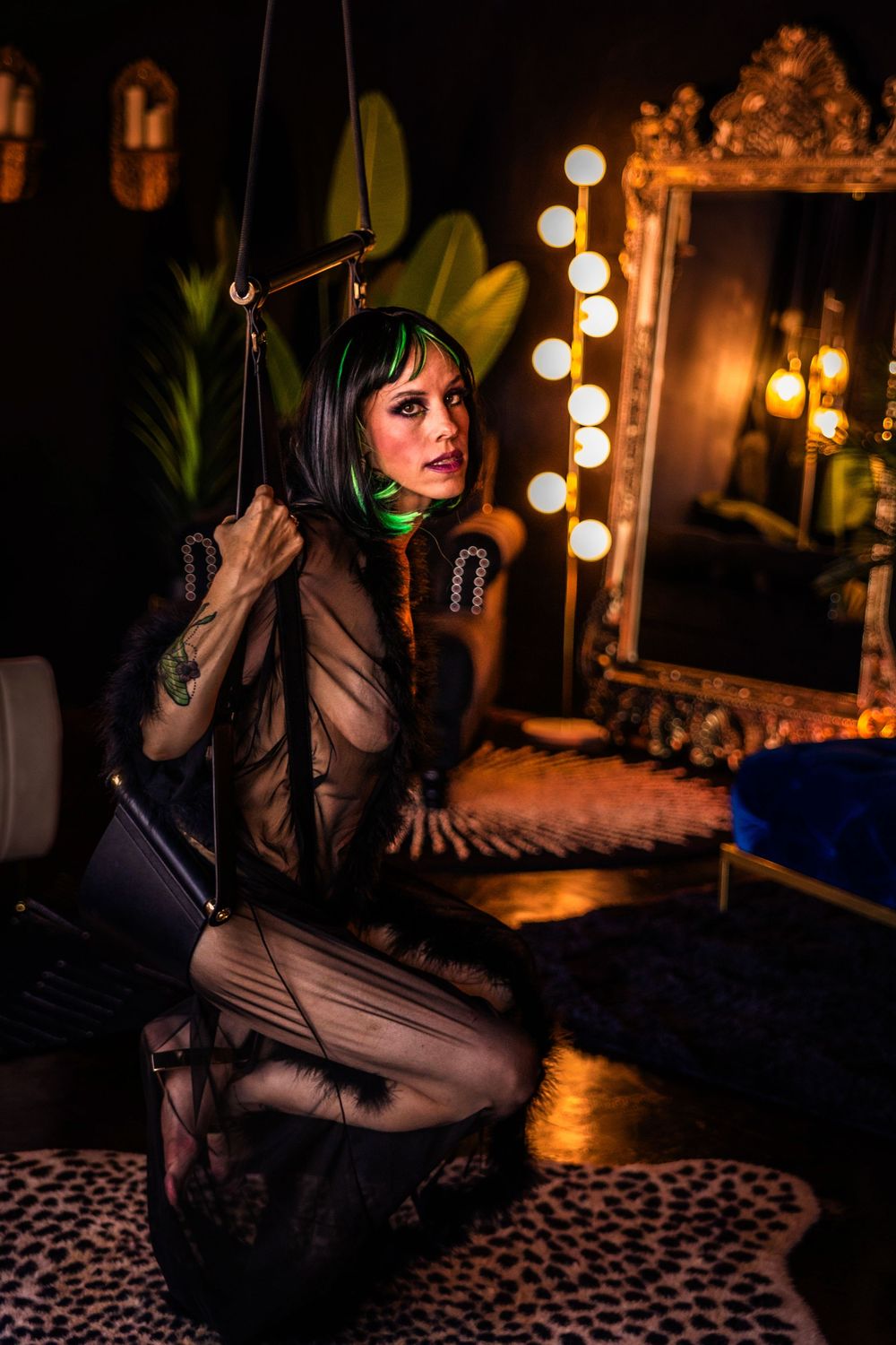 A woman with dark hair poses in a swing. She is wearing a shear robe.