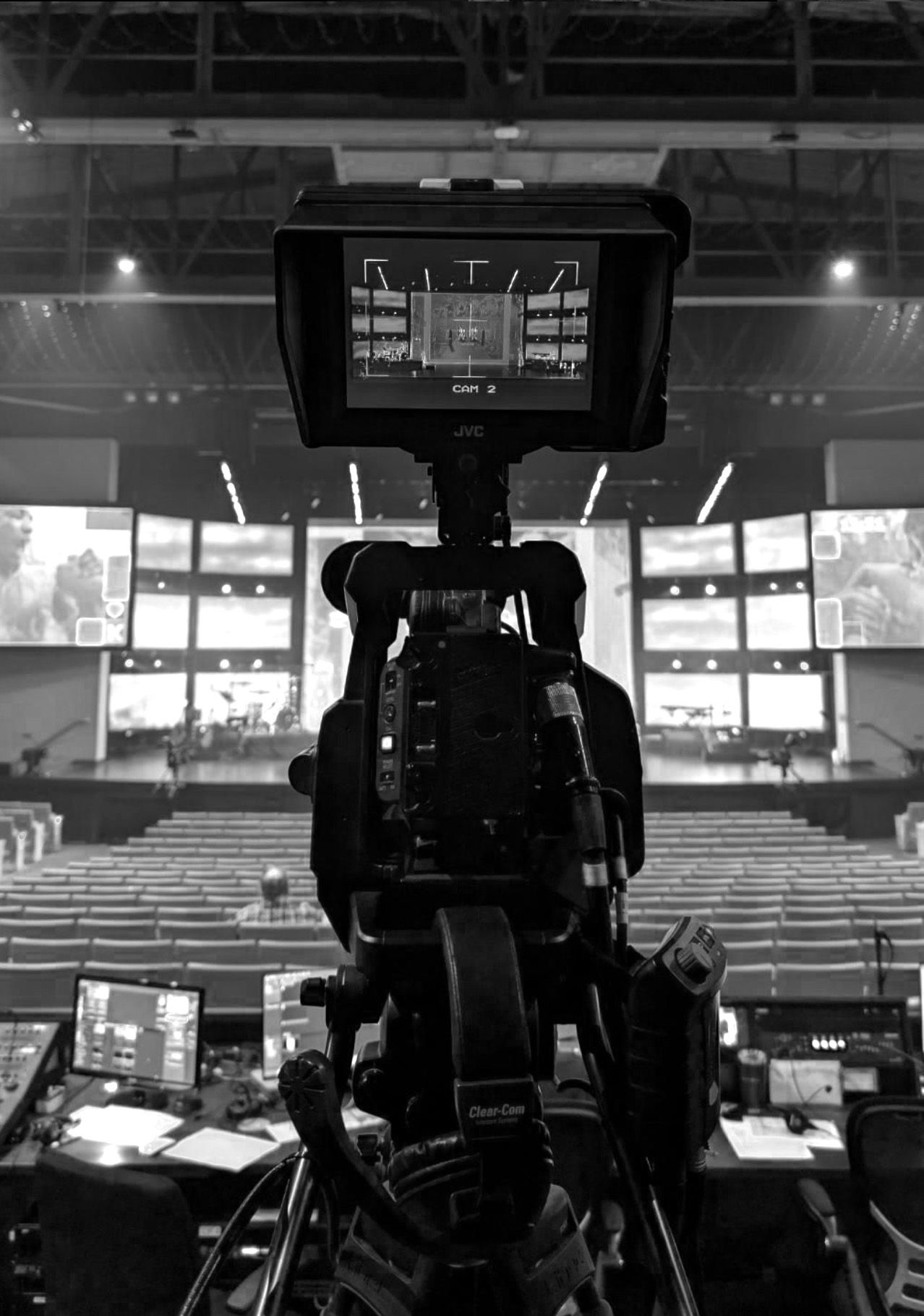 Professional video camera setup in dark arena with multiple display screens in background.