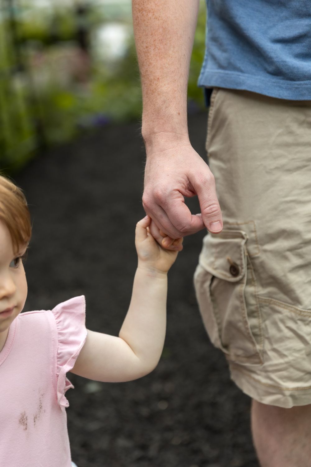 Adult and child holding hands while walking together outdoors.