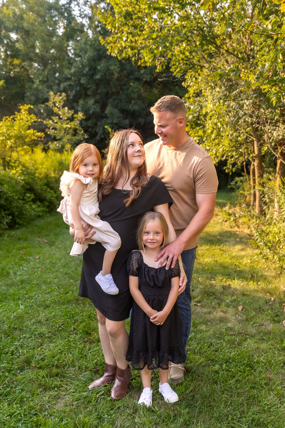Family of four poses together outdoors against lush green foliage background.