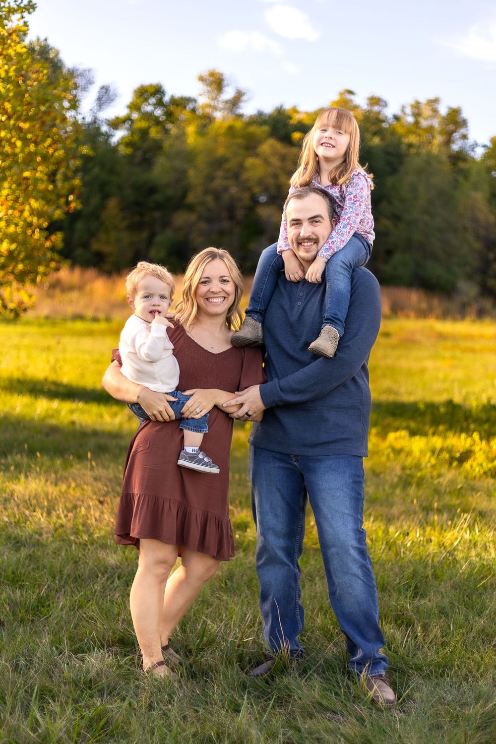 Family enjoying an autumn photo session together in a sunlit field with golden foliage in the background.
