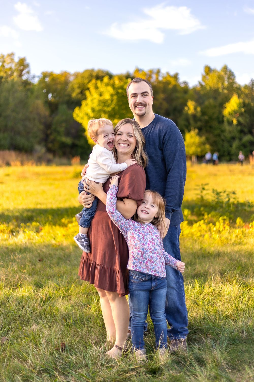 Casual outdoor family portrait with warm autumn colors and natural golden lighting in a grassy field.
