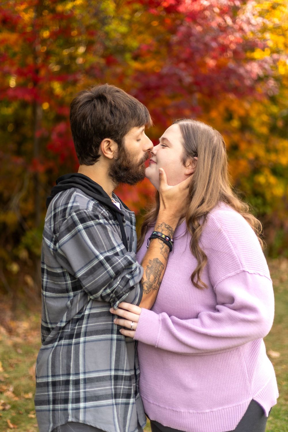 A romantic embrace captured during an autumn photoshoot with colorful trees in background.
