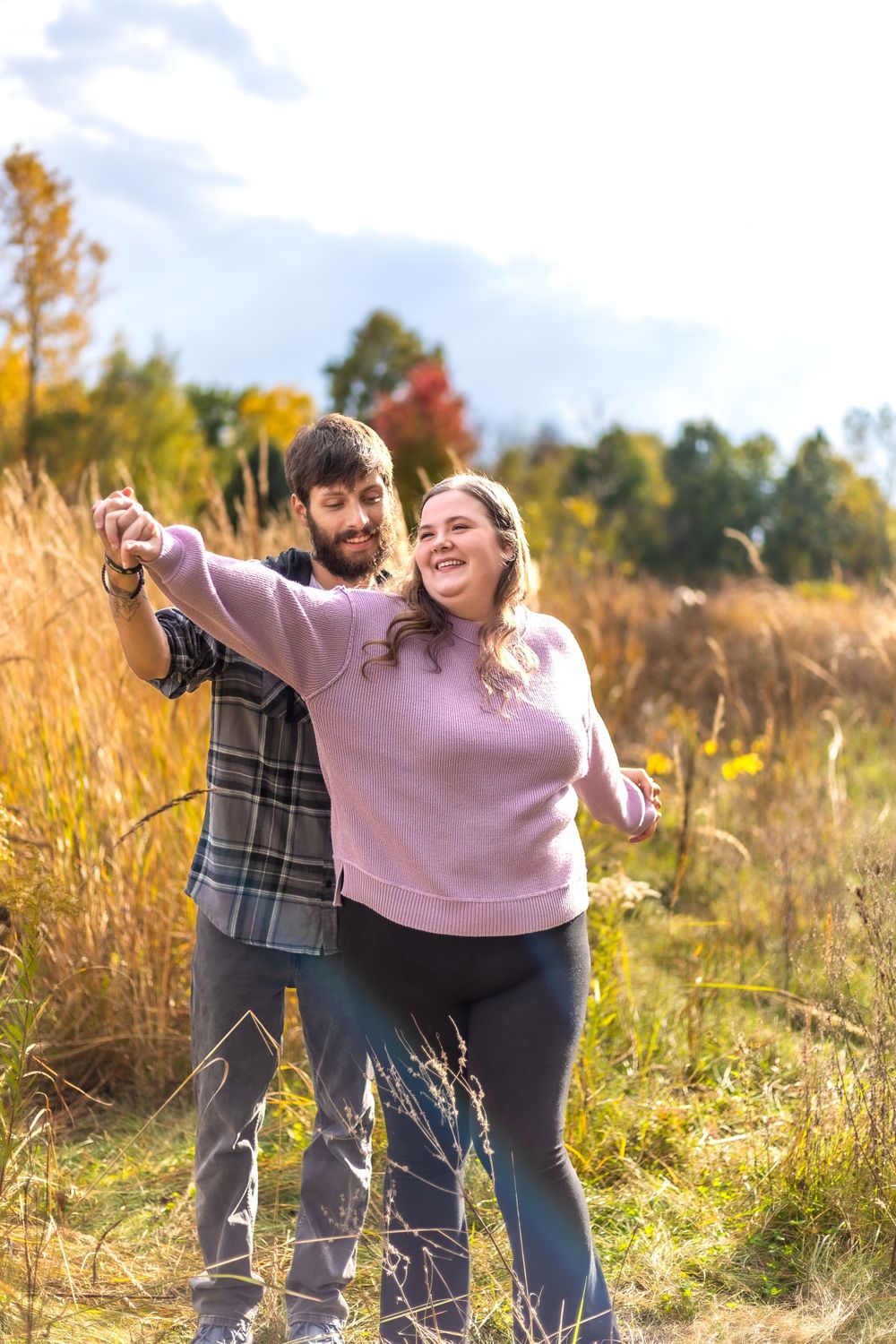 A couple poses playfully in a sunlit autumn field with golden grasses.