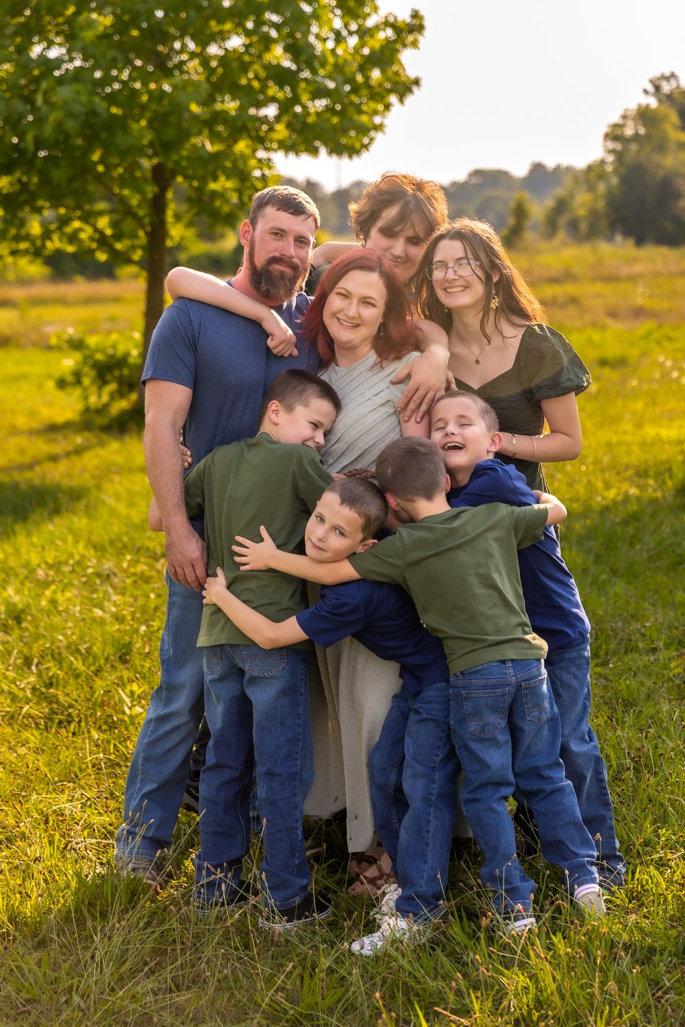 Family embraces while laughing together in a golden autumn field during sunset.