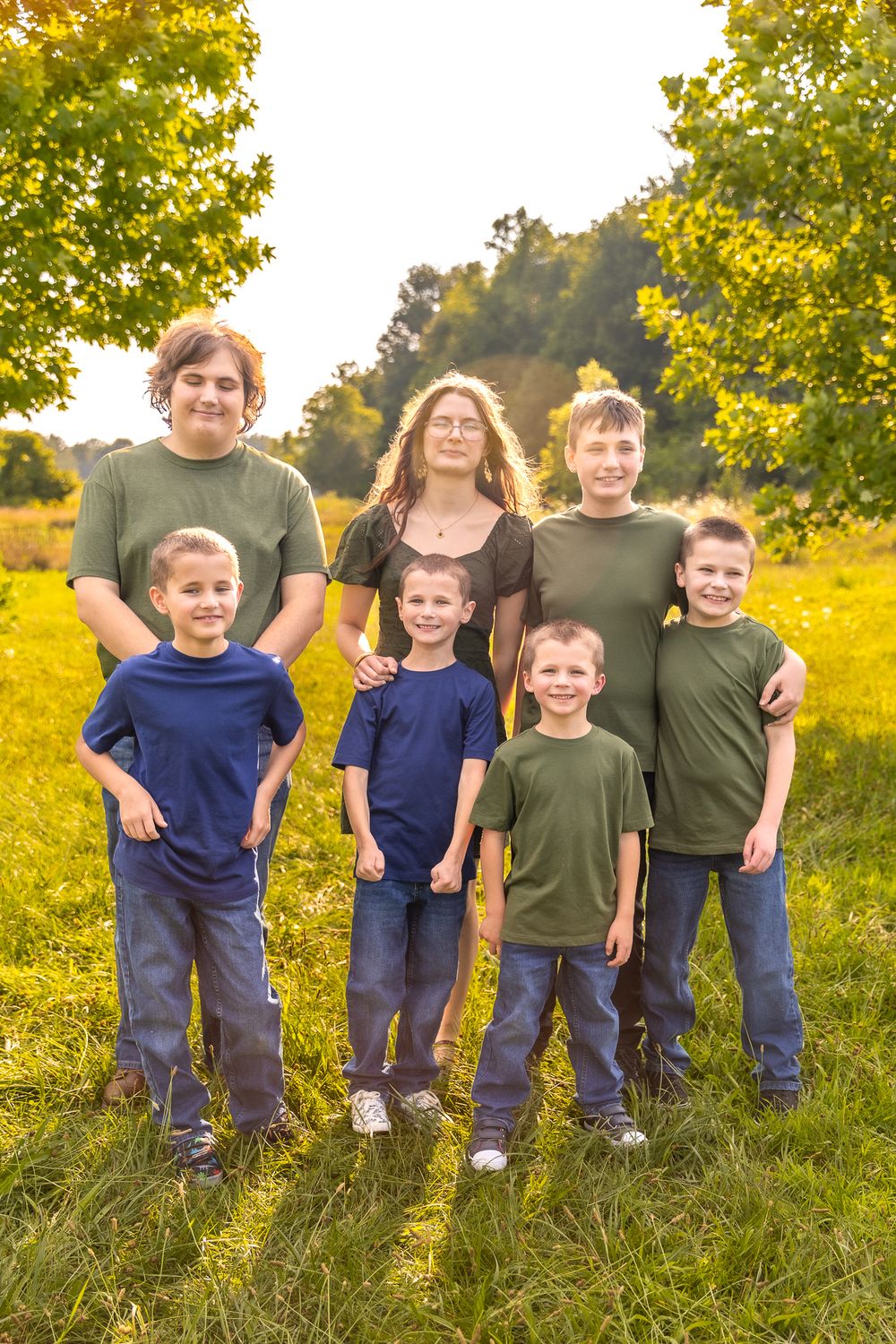 Children and adults stand together in matching blue and green outfits against a golden autumn field and trees.