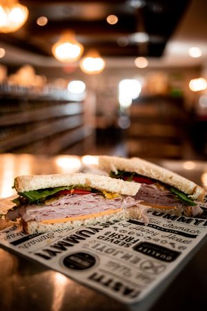 Close-up shot of sliced deli sandwich on custom printed paper wrapper with blurred warm lighting in background.
