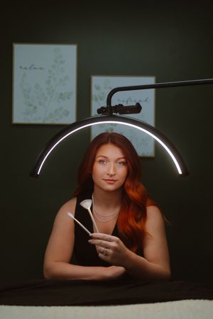 Moody creative portrait lit by curved ring light with artistic lighting and shadows against dark wall.
