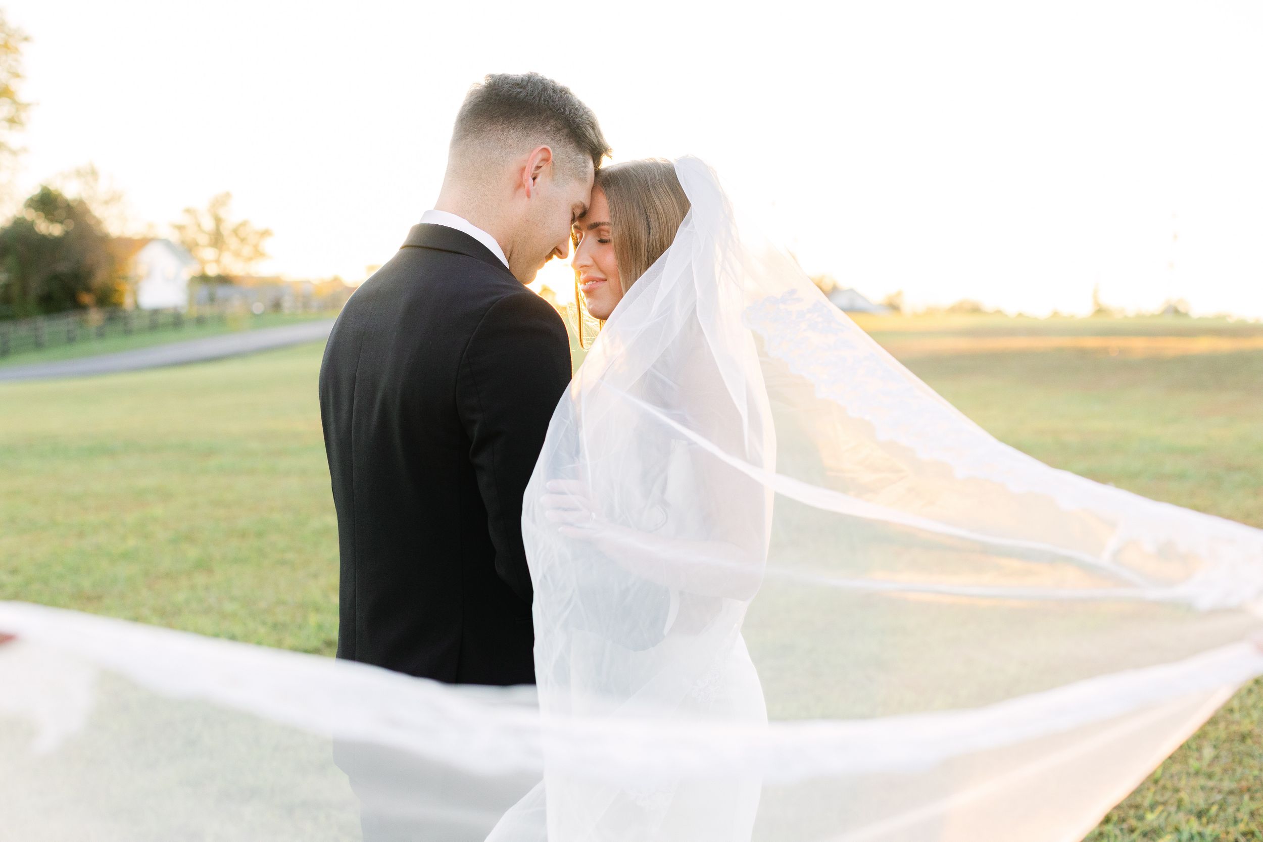 Bride and groom sharing a romantic moment holding a white floral bouquet with greenery on their wedding day.