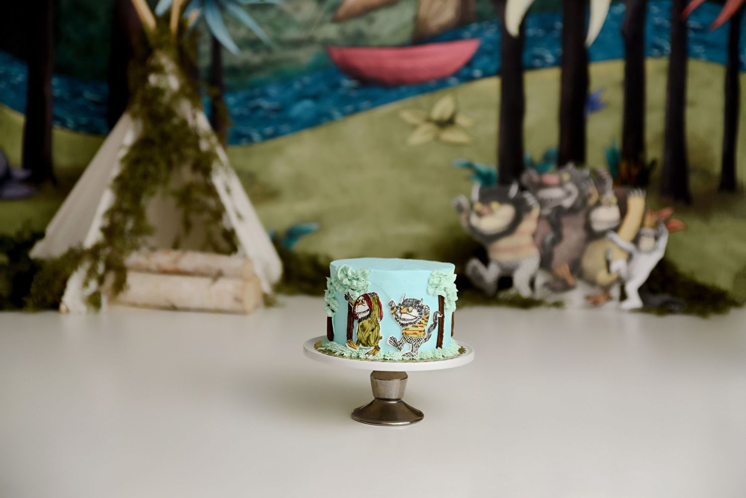 Blue Where the Wild Things Are smash cake with illustrated character backdrop and teepee.