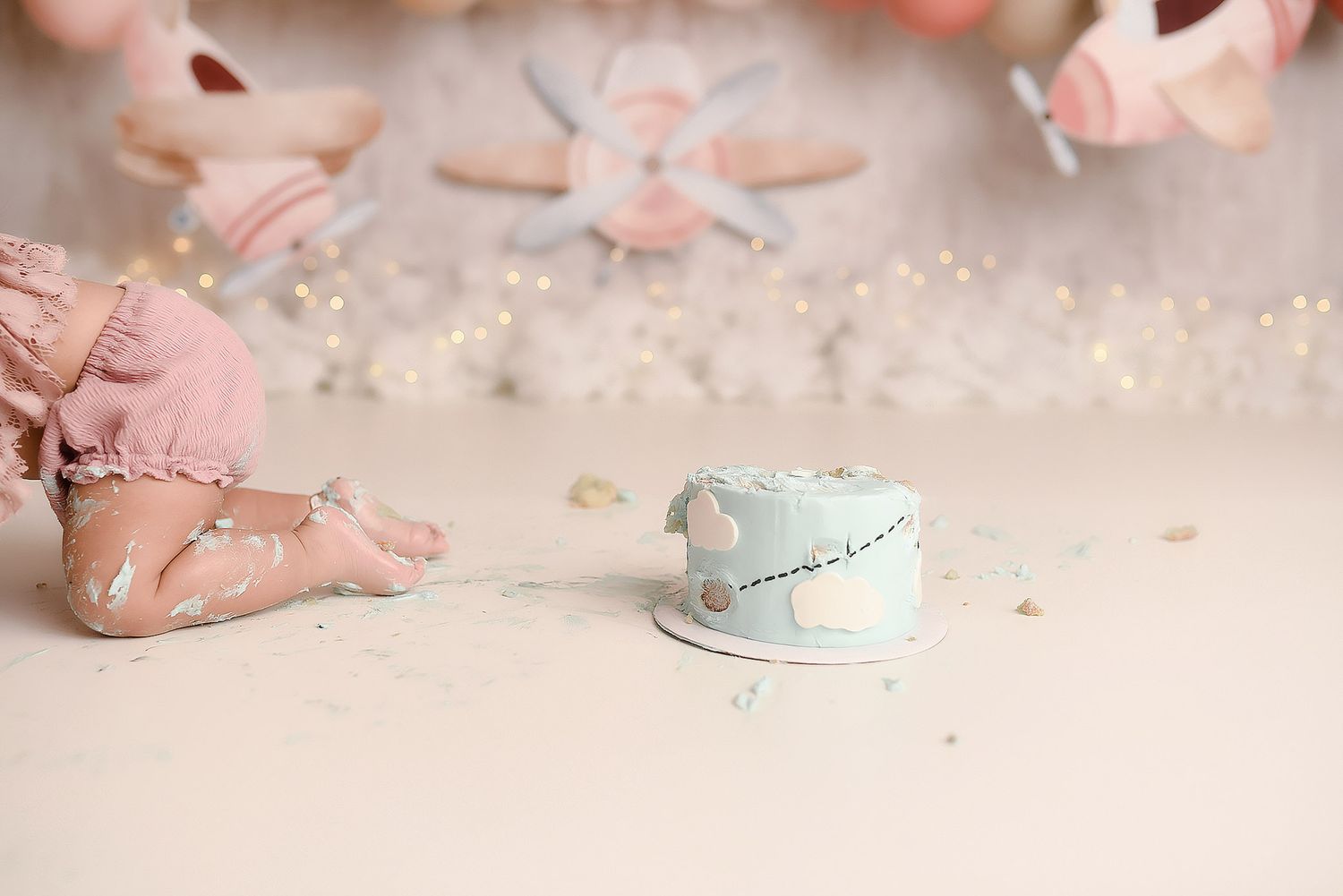 Close-up of baby feet beside smashed light blue birthday cake on white floor.