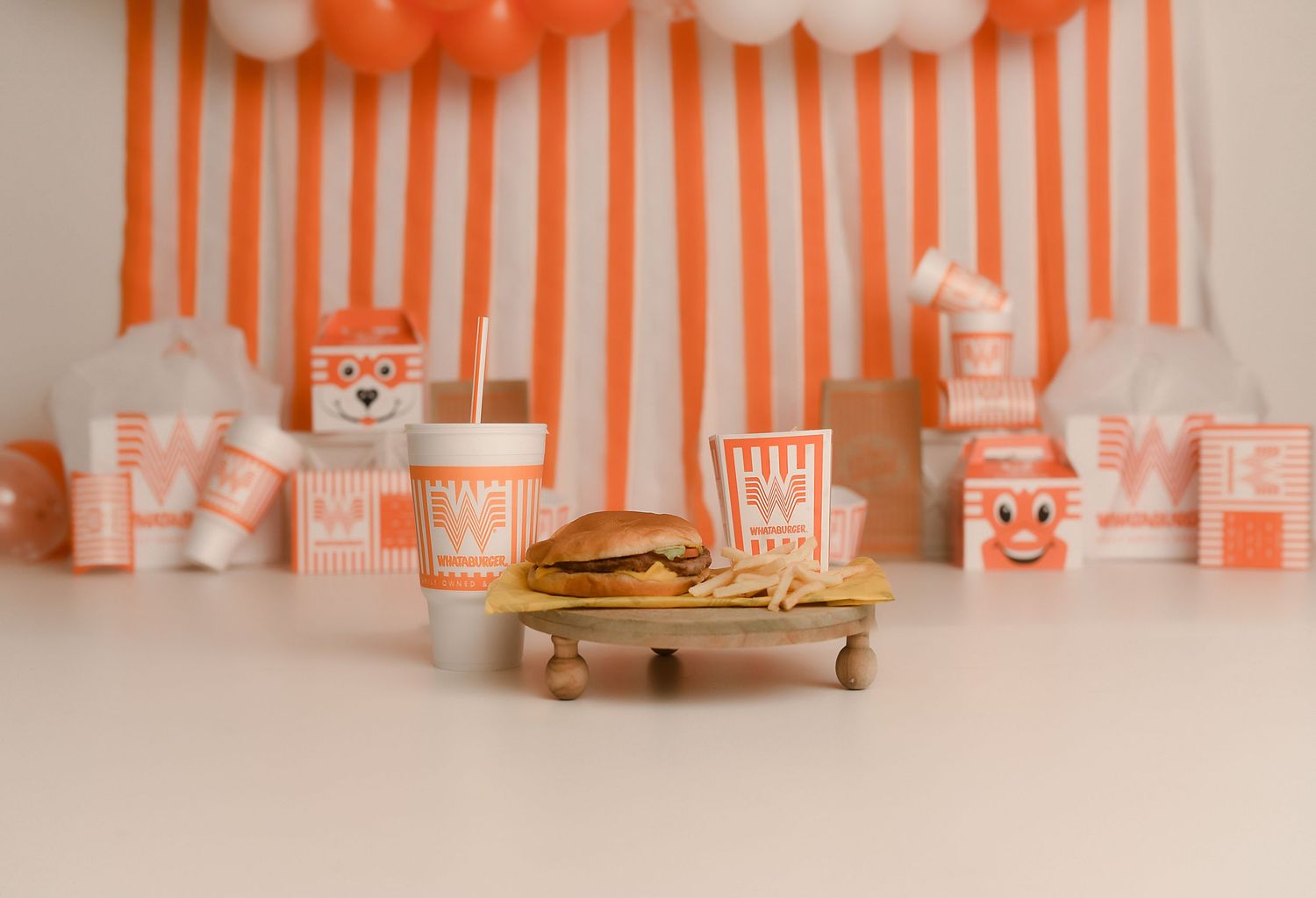 Orange and white striped party setup with burger, fries, cups, and boxes on a miniature wooden tray.