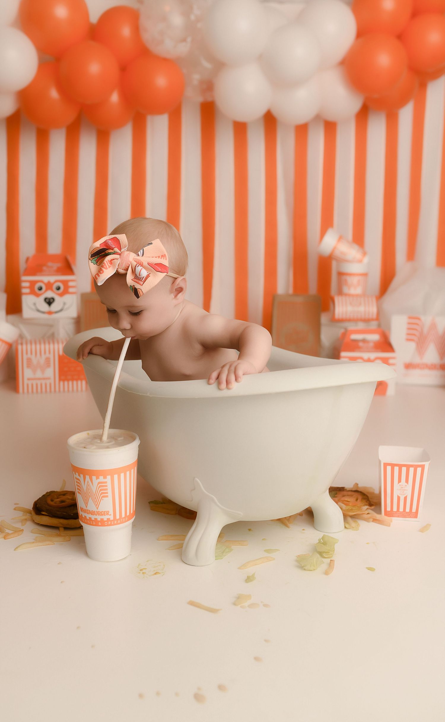 Baby in mini bathtub sipping drink at orange and white themed first birthday cake smash photo shoot.