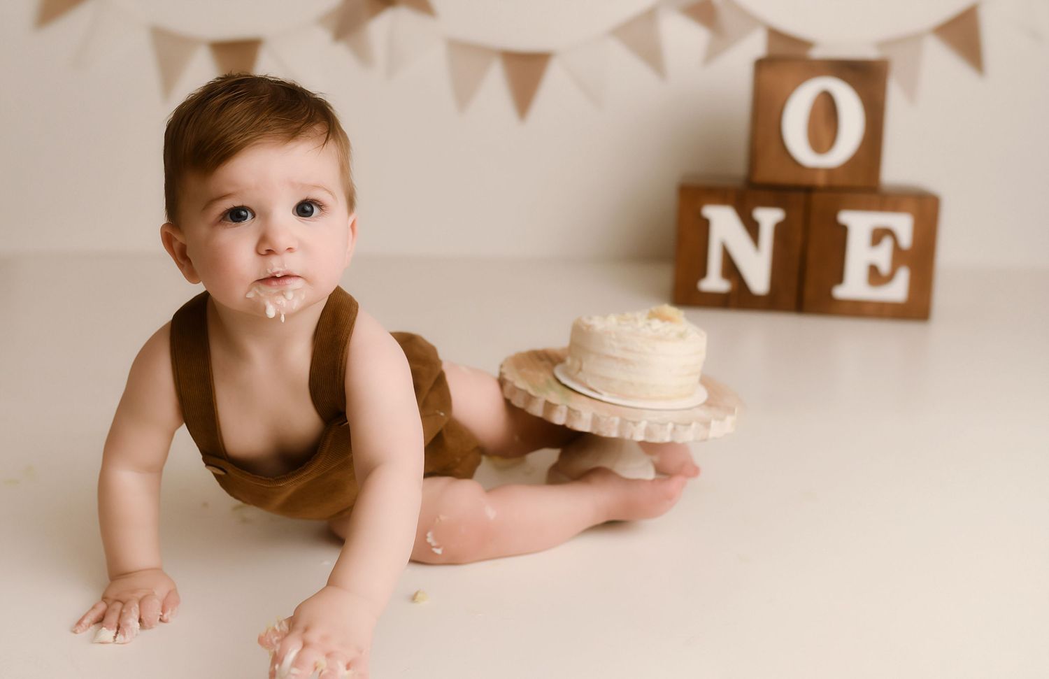 Baby's first birthday cake smash photo with ONE blocks, brown romper, and white cake on white background.
