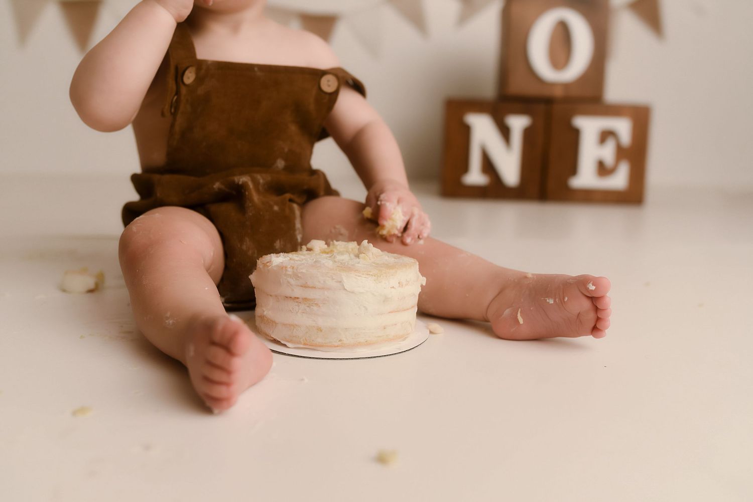 Baby in brown romper smashing first birthday cake during one year cake smash photo session.