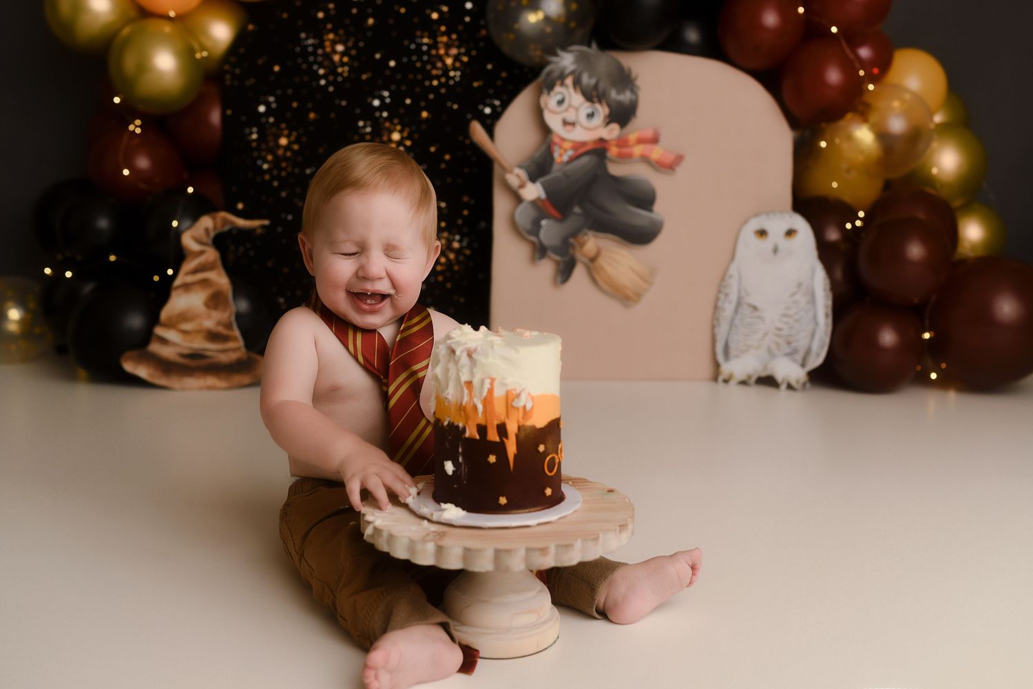 Baby's first birthday cake smash with Harry Potter theme, balloons, and owl backdrop.