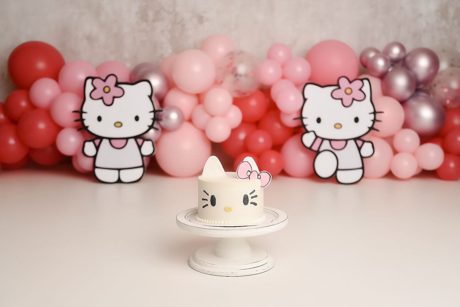 Hello Kitty themed first birthday cake with pink balloons and Hello Kitty cutout decorations.